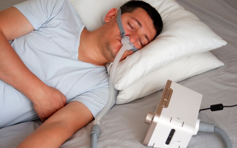 Hombre durmiendo con una mascarilla nasal conectada a un CPAP, utilizado para mantener la respiración estable durante el sueño
