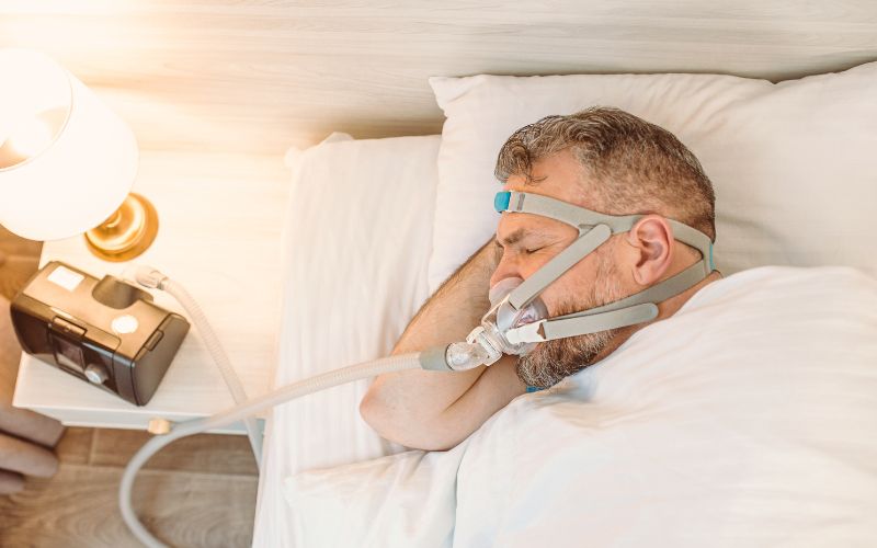 Hombre dormido con mascarilla CPAP, tratamiento que puede ser temporal o permanente según el diagnóstico y evolución del paciente
