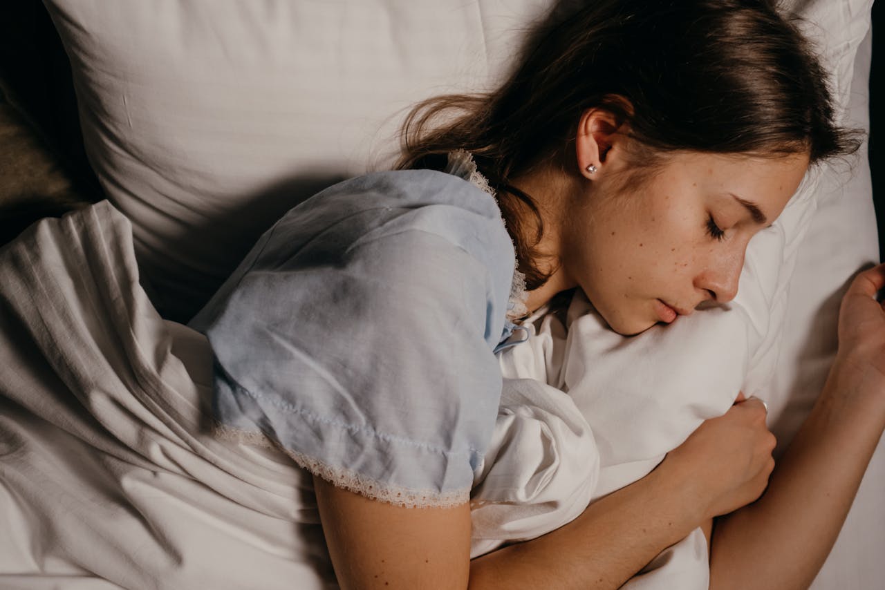 Mujer durmiendo plácidamente en cama blanca, representando descanso profundo y sueño reparador.