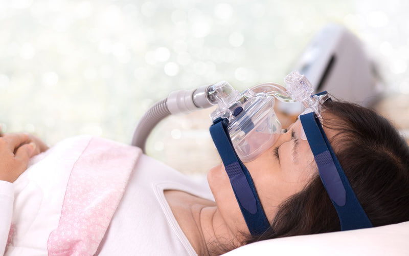 Persona durmiendo con mascarilla y equipo CPAP ajustado para tratar la apnea del sueño con presión controlada.