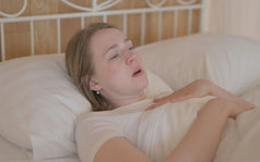 Mujer acostada en la cama con expresión de angustia y respiración agitada, experimentando sensación de ahogo al dormir